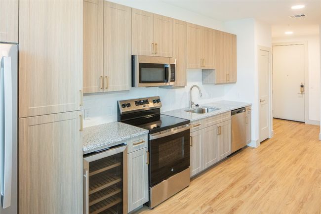 Kitchen featuring light wood finished floors, beverage cooler, visible vents, appliances with stainless steel finishes, and a sink | Image 8