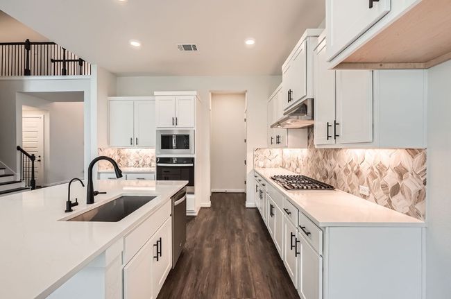 Kitchen with a sink, appliances with stainless steel finishes, under cabinet range hood, dark wood-type flooring, and white cabinets | Image 9