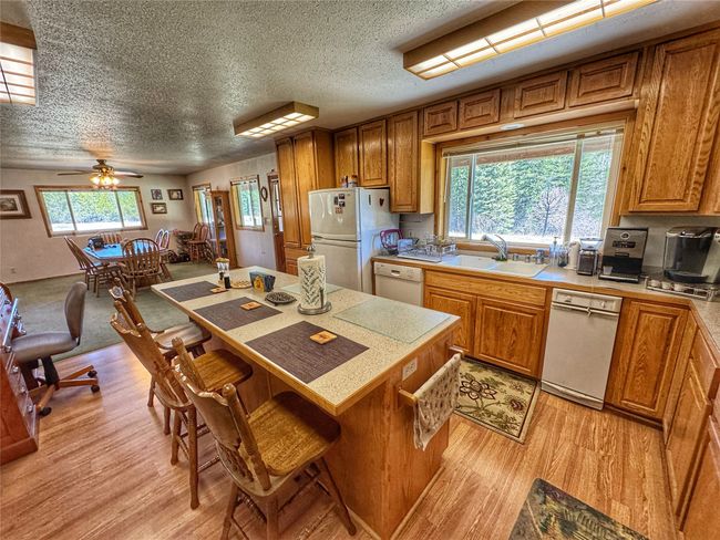 Kitchen with brown cabinetry, white appliances, a kitchen breakfast bar, and a textured ceiling | Image 15