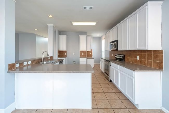Kitchen with visible vents, appliances with stainless steel finishes, white cabinets, a sink, and a peninsula | Image 21
