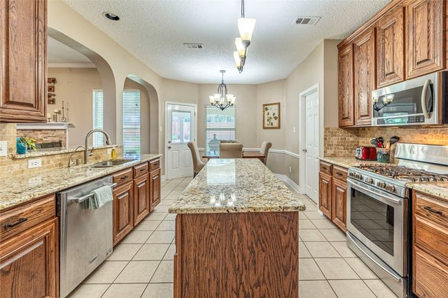 Kitchen featuring stainless steel appliances, a sink, brown cabinets, arched walkways, and a textured ceiling | Image 18