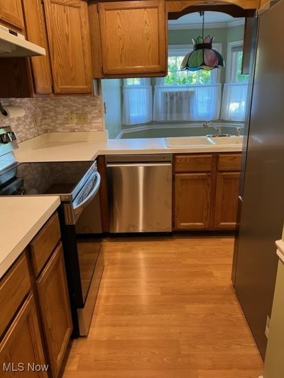 Kitchen featuring ornamental molding, tasteful backsplash, light hardwood / wood-style flooring, sink, and appliances with stainless steel finishes | Image 3