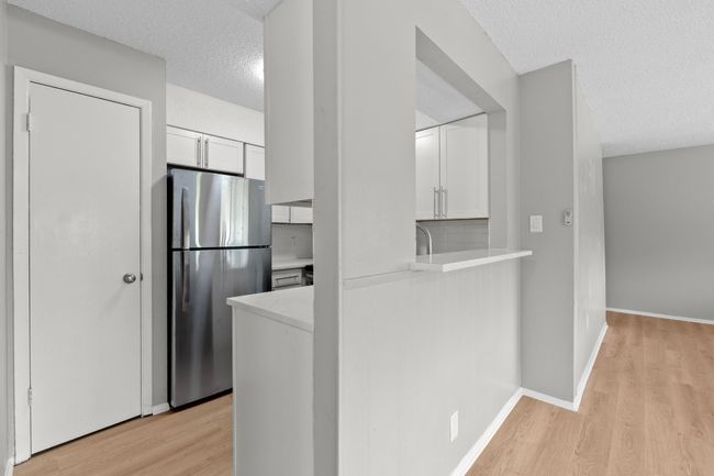 Kitchen with a textured ceiling, light wood finished floors, light countertops, white cabinetry, and freestanding refrigerator | Image 9