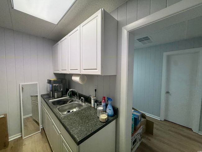 Kitchen with light wood-type flooring, dark countertops, white cabinets, a paneled ceiling, and wooden walls | Image 8