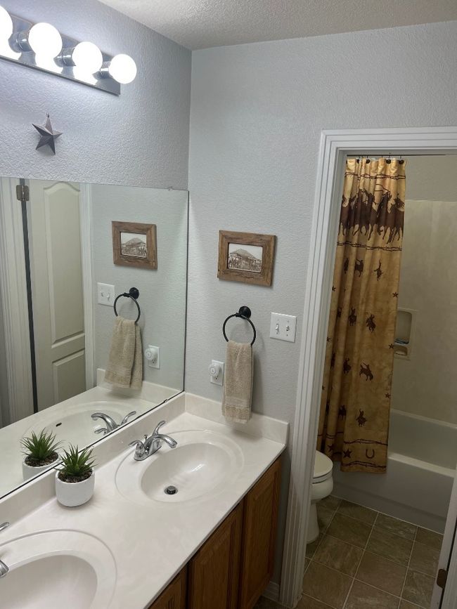 Bathroom with double vanity, shower / bath combo, a textured wall, and a textured ceiling | Image 12