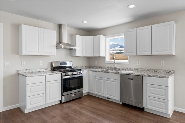 Kitchen featuring white cabinetry, stainless steel appliances, a sink, dark wood-style floors, and wall chimney exhaust hood | Image 34