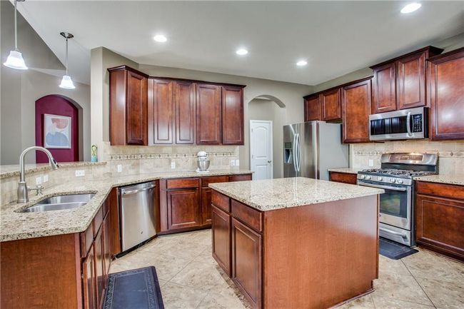 Kitchen with appliances with stainless steel finishes, arched walkways, backsplash, light stone counters, and pendant lighting | Image 10