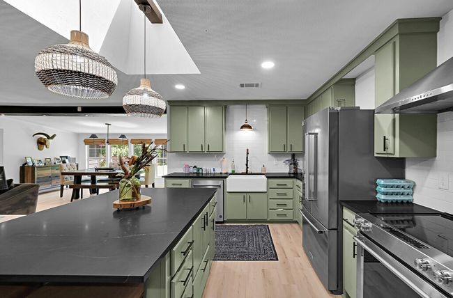 Kitchen featuring stainless steel appliances, green cabinetry, wall chimney exhaust hood, a barn door, and recessed lighting | Image 6