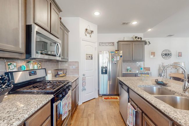 Kitchen with light wood-style flooring, light stone countertops, decorative backsplash, stainless steel appliances, and a sink | Image 8