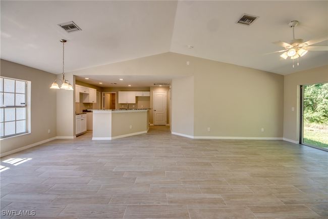 Unfurnished living room featuring lofted ceiling, baseboards, visible vents, and ceiling fan with notable chandelier | Image 15
