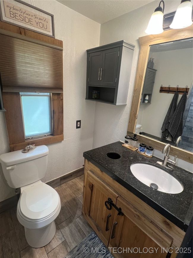 Half bathroom with toilet, wood finished floors, a textured wall, vanity, and baseboards | Image 16