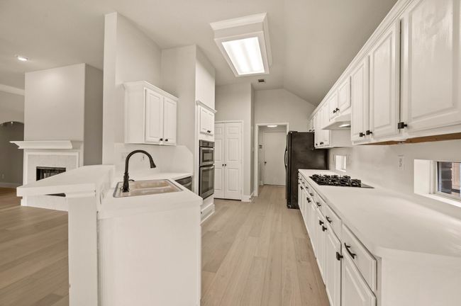 Kitchen with light wood-style flooring, a peninsula, lofted ceiling, white cabinetry, and a sink | Image 14
