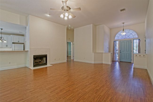 Unfurnished living room with ceiling fan, light wood-style flooring, a fireplace, and a high ceiling | Image 7