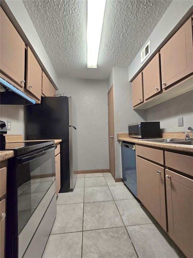 Discover a sleek galley kitchen with elegant cabinetry, a modern electric stove, and a convenient dishwasher. Enjoy bright, efficient lighting and easy-care tiled floors. | Image 14
