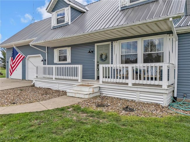Property entrance featuring metal roof, concrete driveway, a garage, and covered porch | Image 6