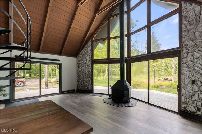Unfurnished living room with high vaulted ceiling, healthy amount of natural light, wood ceiling with exposed beams, a wood stove, and wood finished floors | Image 12
