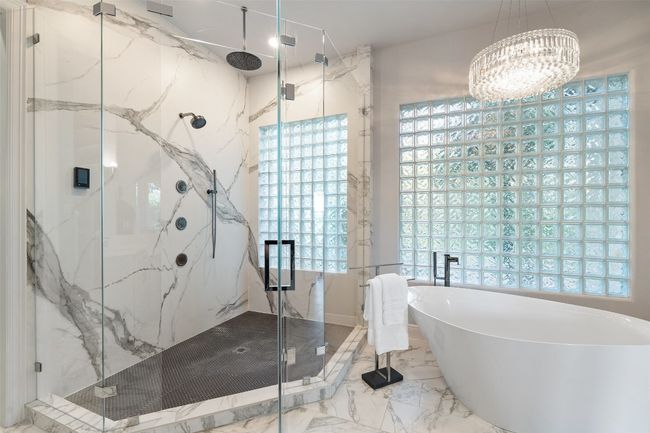 Bathroom featuring marble tiled floors, a soaking tub, a marble finish shower, and a chandelier | Image 21