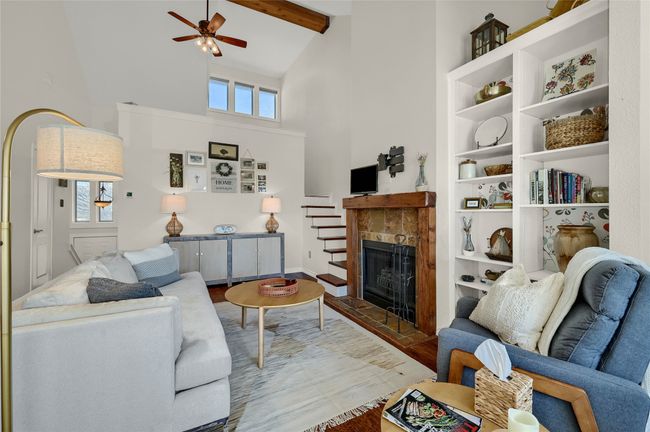 Living area featuring high vaulted ceiling, ceiling fan, wood finished floors, a fireplace with raised hearth, and plenty of natural light | Image 5