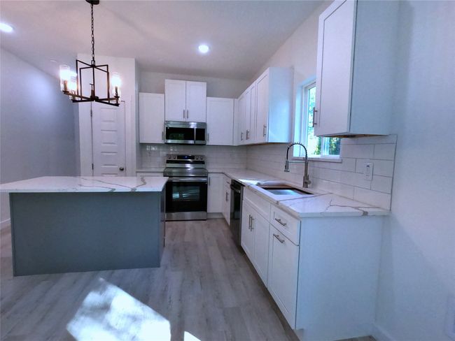 Kitchen with light stone counters, an inviting chandelier, stainless steel appliances, and a sink | Image 4