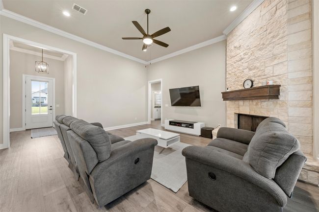 Living room featuring ceiling fan with notable chandelier, light wood-style flooring, ornamental molding, visible vents, and baseboards | Image 5