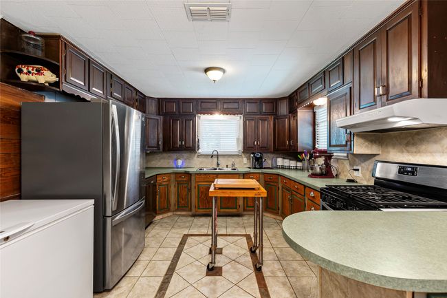 Kitchen featuring under cabinet range hood, appliances with stainless steel finishes, inlaid floor details, light tile patterned floors, and backsplash | Image 4