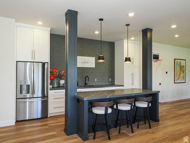 Kitchen featuring stainless steel fridge, white cabinetry, a kitchen breakfast bar, recessed lighting, and light wood-style flooring | Image 72
