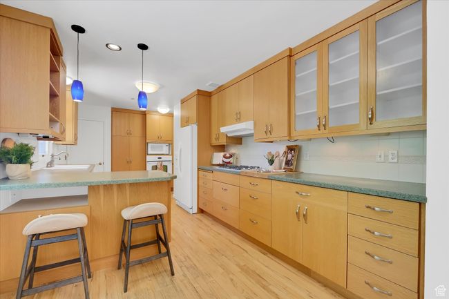 Kitchen featuring white appliances, under cabinet range hood, light wood-style flooring, a peninsula, and open shelves | Image 11