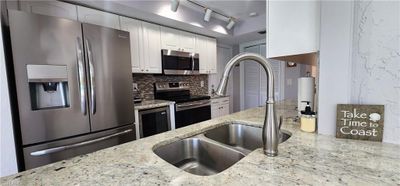 Kitchen featuring light stone countertops, appliances with stainless steel finishes, white cabinets, backsplash, and track lighting | Image 2