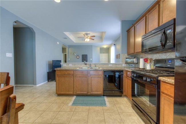 Kitchen featuring black appliances, a tray ceiling, a peninsula, backsplash, and ceiling fan | Image 5