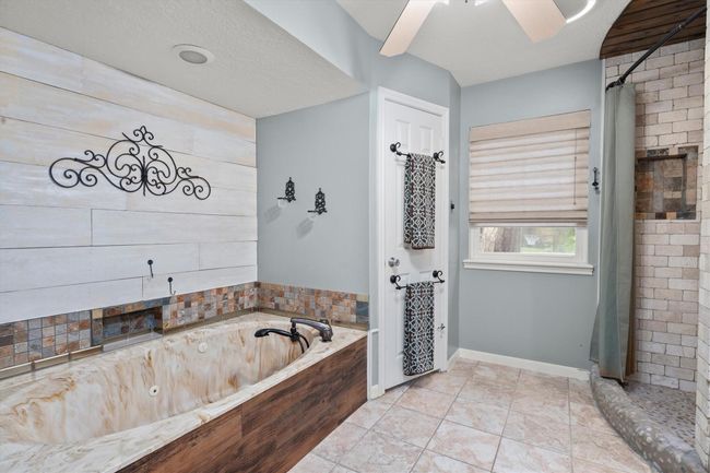 This primary bathroom features a luxurious marble-style jetted tub with a decorative wall accent, a separate tiled shower area, and modern fixtures. Neutral tones and natural light create a serene atmosphere, perfect for relaxation! | Image 27