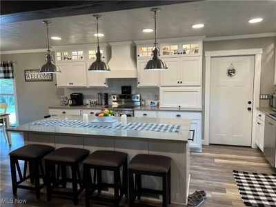 Kitchen featuring appliances with stainless steel finishes, a center island, hardwood / wood-style flooring, white cabinets, and custom range hood | Image 3