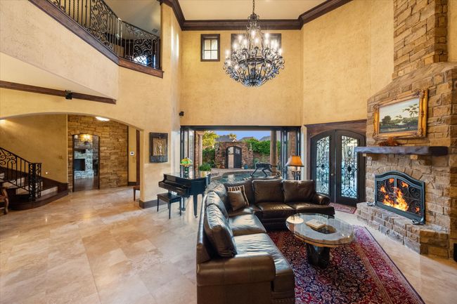 Living area featuring a stone fireplace, a chandelier, arched walkways, a towering ceiling, and ornamental molding | Image 8