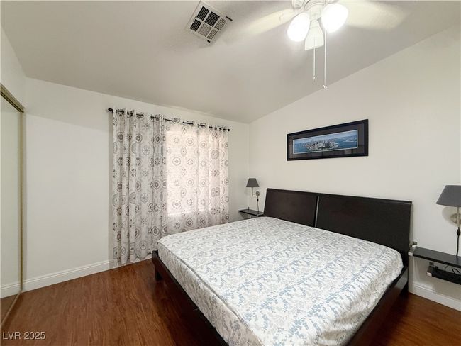 Bedroom with lofted ceiling, wood finished floors, visible vents, a ceiling fan, and baseboards | Image 25