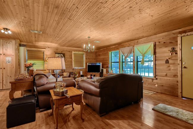 Living room with visible vents, wooden walls, wood finished floors, an inviting chandelier, and wood ceiling | Image 17