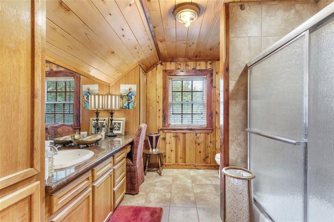 This bathroom features rustic wooden paneling, a spacious vanity with a sink, a cozy seating area, and a shower with sliding doors, creating a warm and inviting atmosphere. | Image 41
