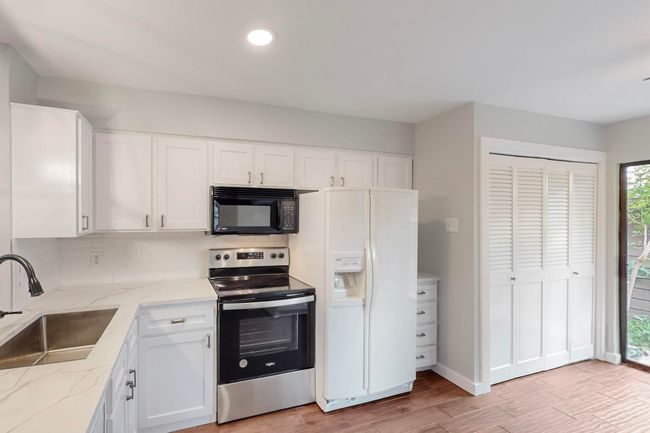 Kitchen with white fridge with ice dispenser, white cabinets, a sink, black microwave, and stainless steel electric stove | Image 13