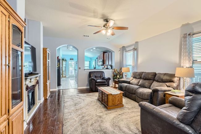Living area with a ceiling fan, arched walkways, baseboards, dark wood-style flooring, and visible vents | Image 6