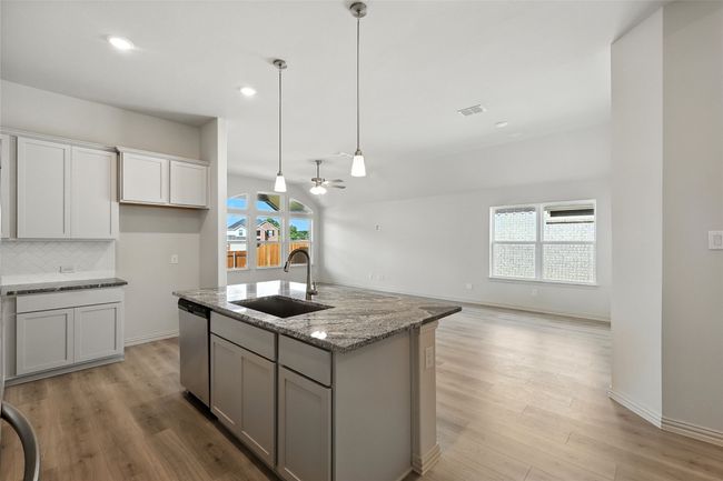 Kitchen with stainless steel dishwasher, ceiling fan, light wood finished floors, decorative backsplash, and light stone counters | Image 4