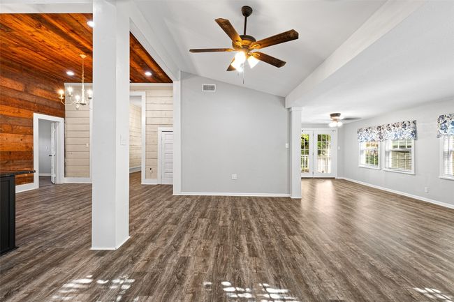 Unfurnished living room with dark wood finished floors, baseboards, ornate columns, ceiling fan with notable chandelier, and lofted ceiling | Image 32