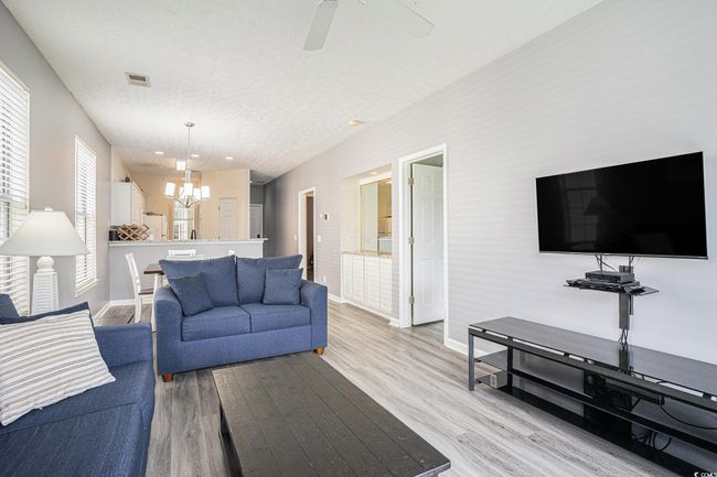 Living area featuring a chandelier, light wood-style flooring, a textured ceiling, and ceiling fan | Image 5