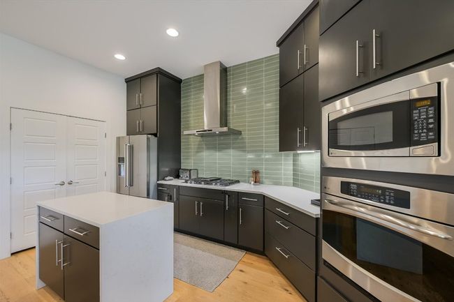 Kitchen featuring stainless steel appliances, wall chimney range hood, light wood-style floors, light countertops, and tasteful backsplash | Image 7