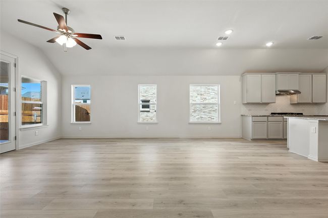 Unfurnished living room featuring lofted ceiling, ceiling fan, healthy amount of natural light, light wood finished floors, and recessed lighting | Image 13