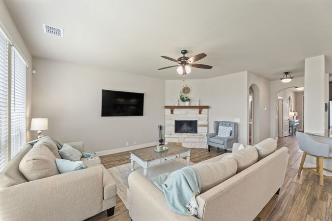 Living room with arched walkways, a ceiling fan, wood finished floors, and a stone fireplace | Image 13