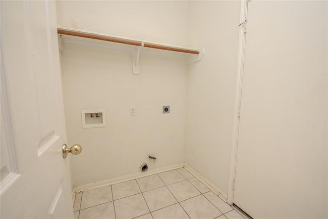 This photo shows a small laundry room with tiled flooring, plumbing hookups, and a shelf for storage. | Image 11