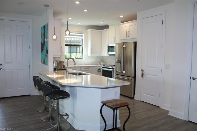Kitchen featuring a breakfast bar area, appliances with stainless steel finishes, a sink, a peninsula, and dark wood-style floors | Image 4
