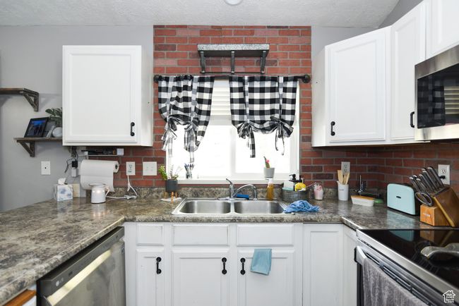 Kitchen featuring a textured ceiling, white cabinetry, tasteful backsplash, a sink, and appliances with stainless steel finishes | Image 17