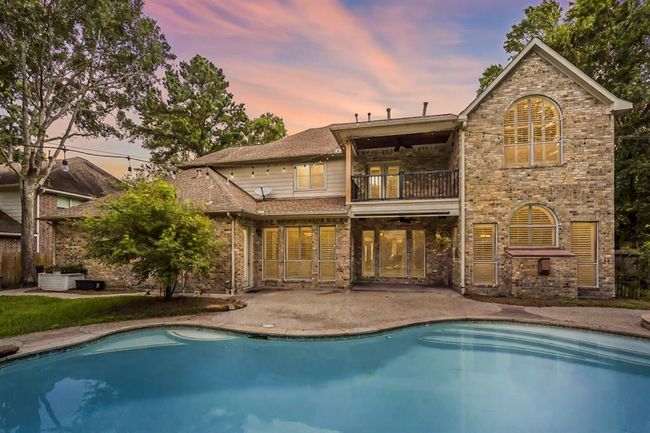 Charming home with a spacious backyard featuring a swimming pool. The house has large windows with shutters, a balcony, and a cozy patio area, set against a serene backdrop of trees. | Image 11