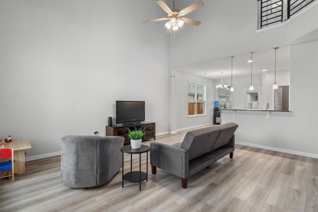 Living area featuring wood finished floors, ceiling fan, baseboards, a chandelier, and a high ceiling | Image 6