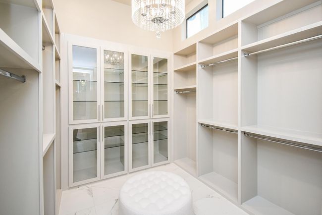 Primary retreat features his and hers separate closets. This is a spacious, elegant walk-in closet "for her" featuring ample shelving, hanging space, glass cabinet doors, and a luxurious chandelier. | Image 31