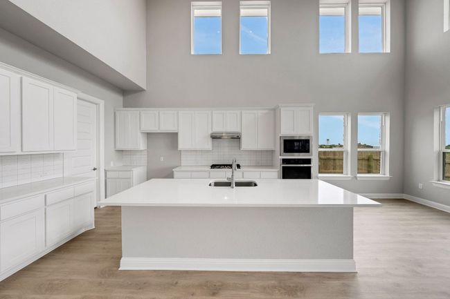 Kitchen featuring backsplash, black oven, white cabinets, light wood finished floors, and a towering ceiling | Image 9
